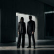 Silhouette d'un homme et d'une femme en costume sombre dans une architecture minimaliste en béton.