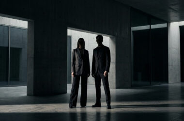 Silhouette d'un homme et d'une femme en costume sombre dans une architecture minimaliste en béton.