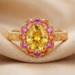 Bague en or gravé avec un saphir jaune ovale entouré de petites pierres roses et orange sur un tissu beige satiné.
