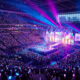 Vue panoramique d'un concert d'EXO avec une foule tenant des bâtons lumineux et une scène illuminée de néons.