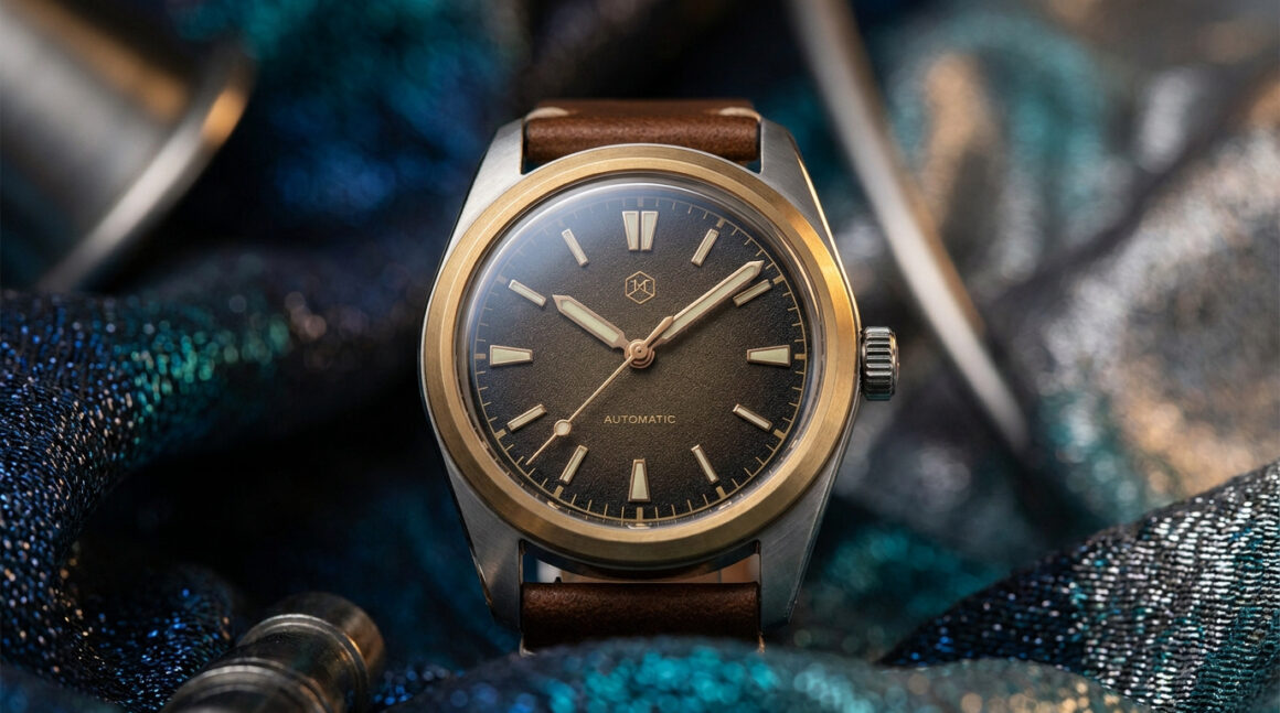 Montre automatique avec cadran marron, lunette dorée et bracelet en cuir, posée sur un tissu bleu brillant.