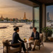 Un couple en discussion sur la terrasse du Capella Bangkok face au fleuve Chao Phraya au coucher du soleil.
