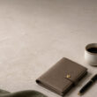Un portefeuille en cuir beige, un stylo et une tasse de café sur une table en pierre claire pour un style minimaliste.